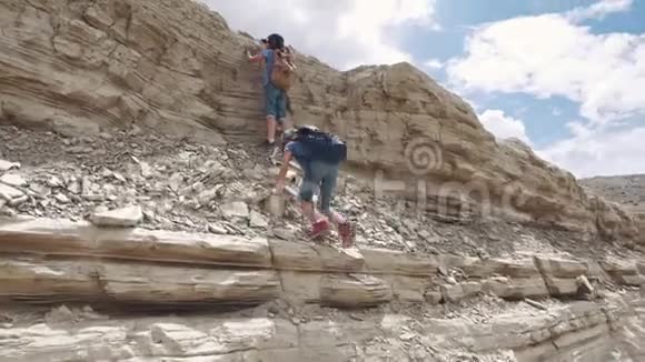 孩子们爬上岩石带背包的小旅行者两个小女孩在山上徒步旅行视频的预览图