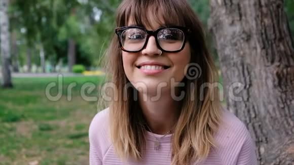 年轻女子对着镜头微笑的肖像公园里漂亮的时髦女孩夏日视频的预览图