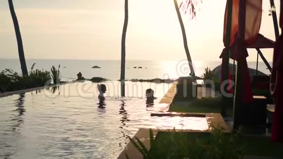 海滩上漂亮的餐厅情侣们的浪漫之地一男一女正在游泳池里游泳日落视频的预览图