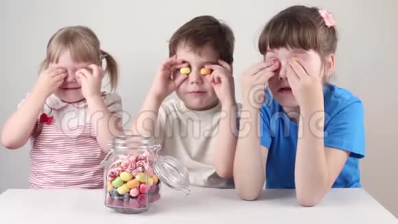 三个快乐的孩子在桌上的罐子附近玩糖果视频的预览图