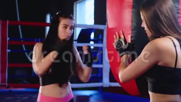 贴身可爱的年轻黑发女子运动员用双手穿着黑色运动绷带在拳击袋上挥拳视频的预览图
