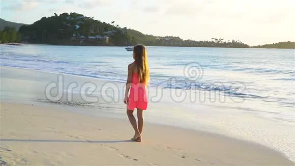 可爱的快乐小女孩在日落时走在白色的海滩上流动电视视频的预览图