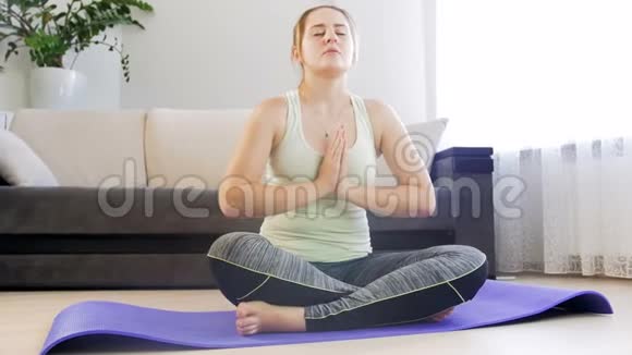 漂亮的年轻女子在客厅的健身垫上冥想和练习瑜伽视频的预览图