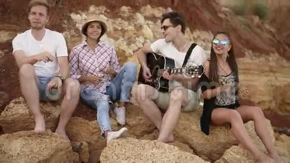 一群年轻的时髦朋友坐在海边的岩石上弹吉他唱歌跳舞视频的预览图