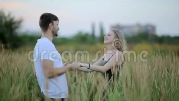 一对恩爱的夫妻男人亲吻一个女人然后开玩笑地丢下她有趣的年轻人和女人牵着手在田野里旋转视频的预览图