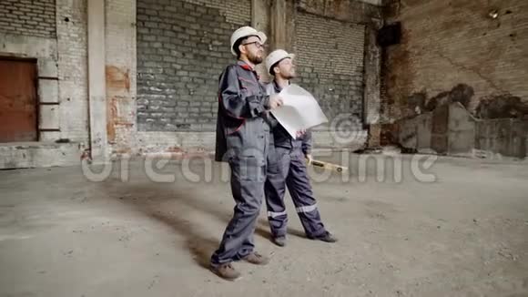 两个穿着制服和安全安全帽的人站在建筑工地上看着工作区福尔曼视频的预览图