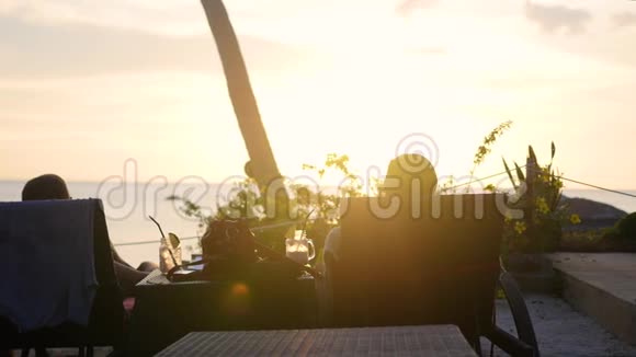 女孩和男孩坐在躺椅上看日落热带岛屿视频的预览图