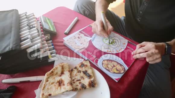 男人坐在咖啡馆里用艺术标记在素描本上描绘印度食物的形象视频的预览图