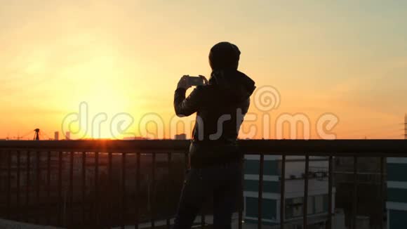 女嬉皮士用手机拍照日落城景屋顶景视频的预览图