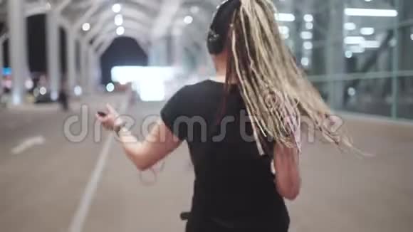 年轻迷人的时髦女性使用智能手机晚上在街上听音乐跳舞视频的预览图