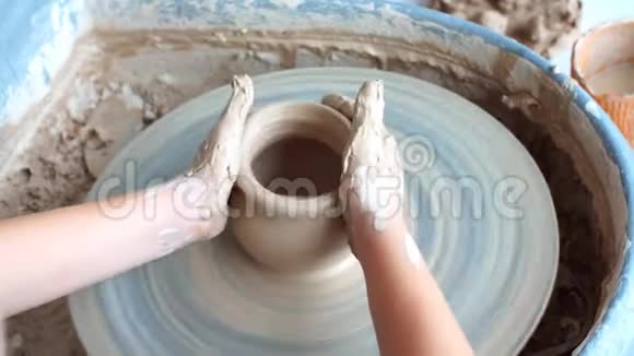 快乐的孩子在车轮上压一个粘土槽孩子在陶轮上慢慢地工作塑造一个花瓶金发的小女孩视频的预览图