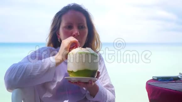 咖啡馆里的小女孩在露台上喝鸡尾酒椰子水露天热带岛屿视频的预览图