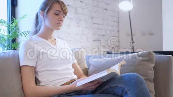 正经的年轻女子坐在沙发上看书视频的预览图