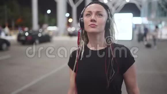 年轻迷人的时髦女性使用智能手机晚上在街上听音乐跳舞视频的预览图