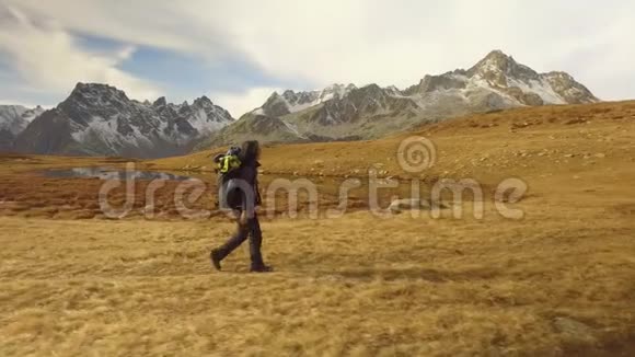 女徒步旅行者走在秋天的田野上靠近湖边的小路到下雪的坐骑从侧面看晴朗的秋日视频的预览图