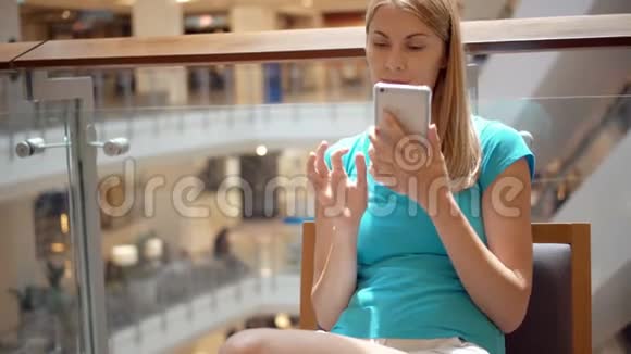 坐在商场广场上的女人用智能手机用智能手机和朋友聊天视频的预览图