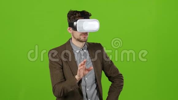 戴着虚拟眼镜的男孩看着想象中的照片和微笑绿色屏幕视频的预览图