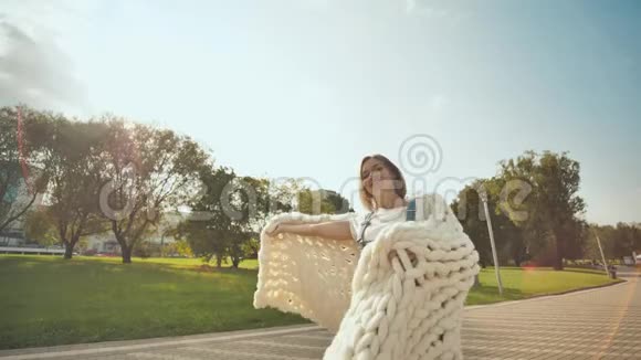 这个快乐的女孩在初秋在公园里挥舞着一个白色的美利奴羊毛格子视频的预览图