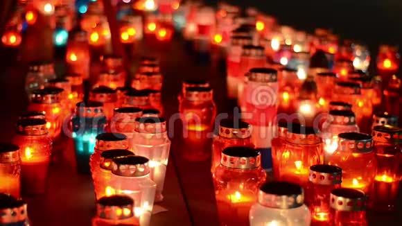 很多五颜六色的蜡烛在晚上在墓地燃烧蜡烛在坟墓上发光所有圣徒日祈祷点燃蜡烛视频的预览图
