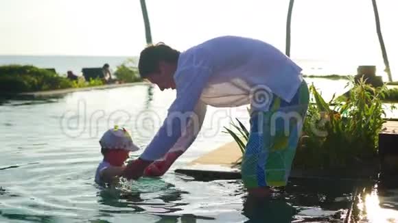 父亲带着一个孩子在海滩旁边的游泳池里玩耍日落时分热带岛屿视频的预览图