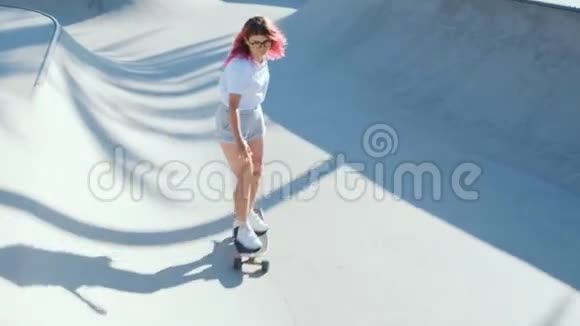 海滩上有粉色头发滑板的漂亮女孩视频的预览图