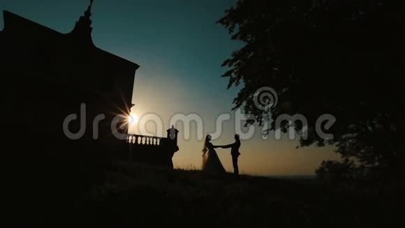 在古堡附近的夕阳下幸福新婚夫妇温柔地牵手亲吻的剪影视频的预览图