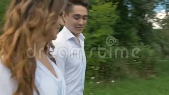 一个年轻的女人和一个穿白色西装的男人在公园里散步握着手在模糊区视频的预览图