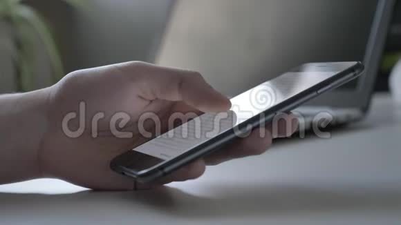 女性手在黑色智能手机上滚动新闻线背景为60fps的笔记本电脑视频的预览图