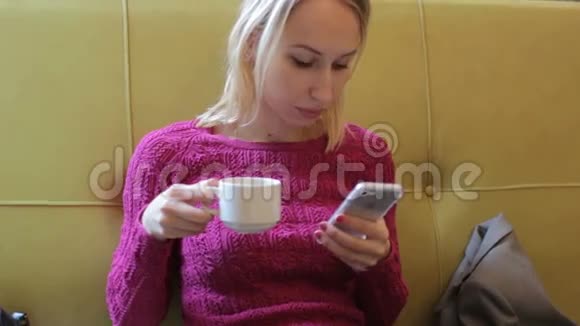 年轻时尚的金发女人在咖啡馆里用智能手机喝茶视频的预览图