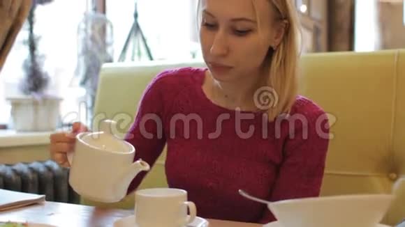 年轻漂亮的金发女人把茶倒在白色的杯子里咖啡厅内部视频的预览图