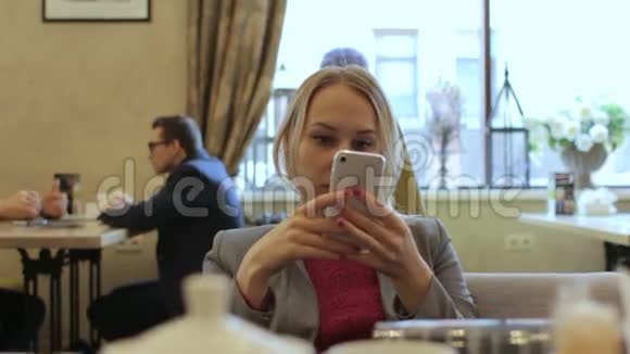 年轻的女商人用智能手机看新闻在咖啡馆工作面带微笑视频的预览图