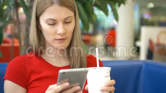 女人坐在咖啡馆里用她的智能手机和朋友聊天喝着纸杯里的可乐视频的预览图