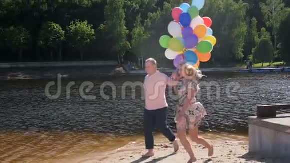 一对快乐的年轻夫妇带着一大堆气球跑步的慢动作视频视频的预览图