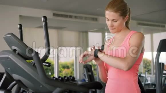 适合积极运动的女人在天鹅绒模拟器上做运动利用她的智能手表检查生命体征视频的预览图