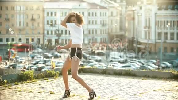 一个穿着小短裤的年轻女子在屋顶上表演迷人的性感舞蹈日落视频的预览图