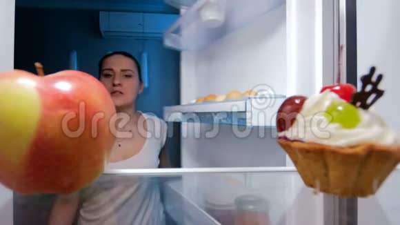 4K镜头年轻女子在夜里寻找食物从冰箱里取出新鲜苹果视频的预览图