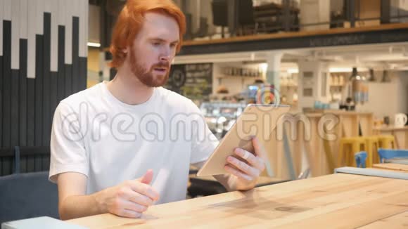 兴奋的红头胡子男庆祝成功坐在咖啡厅视频的预览图