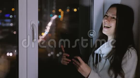 女人用平板电脑做视频聊天和笑夜深人静的坐在窗台上视频的预览图