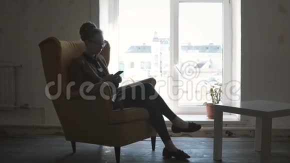 漂亮的年轻女人戴着眼镜坐在黄色的椅子上用智能手机工作视频的预览图