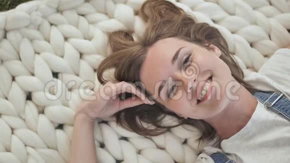 一个年轻的女孩躺在公园里的美利奴白色毯子上享受夏天的天气视频的预览图