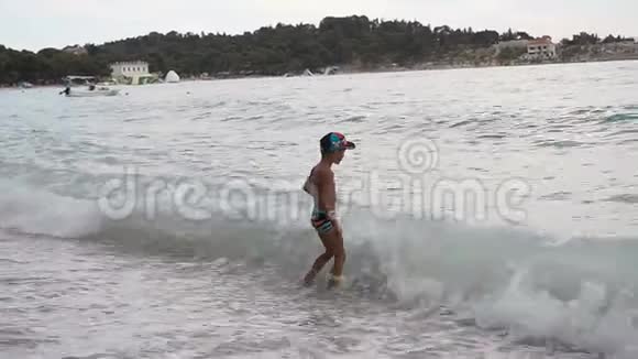 一个好孩子站在亚得里亚海的海滩上快乐地逃离直冲他的巨浪视频的预览图