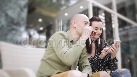 男人和女人在街头咖啡馆喝茶看智能手机上的照片视频的预览图
