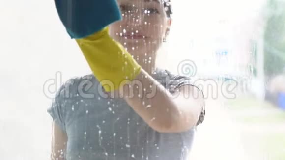 戴着黄手套的漂亮女人用抹布和洗涤剂洗窗户视频的预览图