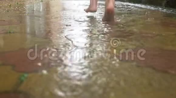 夏雨赤脚穿过水坑温暖的雨雨滴慢动作视频的预览图