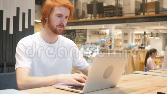 兴奋的红头胡子男庆祝成功坐在咖啡厅视频的预览图