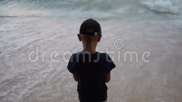 一个穿着深色衣服和帽子的好小家伙站在海边看着汹涌的亚得里亚海视频的预览图