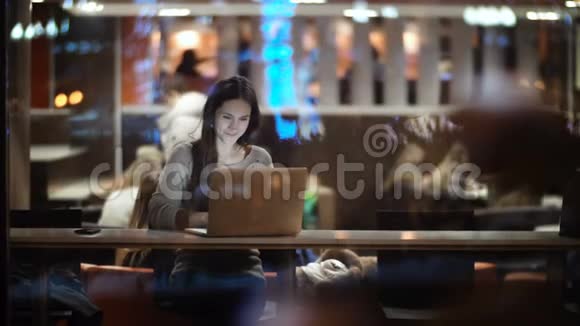 年轻漂亮的女人坐在桌子旁用笔记本电脑从窗口可以看到在咖啡馆工作的女性视频的预览图