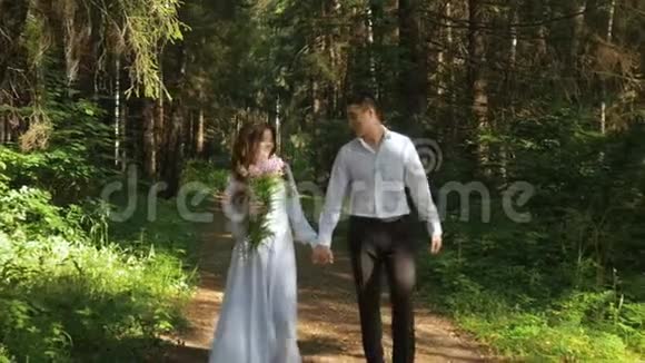 新娘穿着白色连衣裙未婚夫正在森林里散步视频的预览图