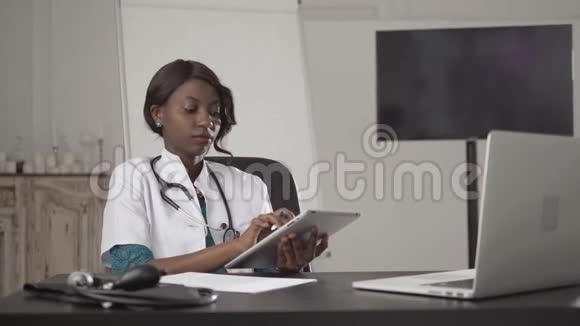 颇具吸引力的非洲医生在电话中用笔记本电脑工作在内阁医院写诊断报告视频的预览图
