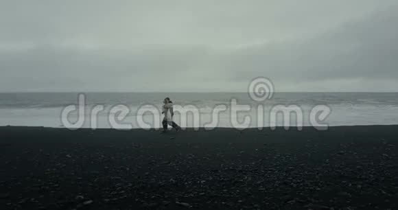 年轻夫妇在黑色火山海滩散步的鸟瞰图男人和女人在冰岛的海边有个约会视频的预览图